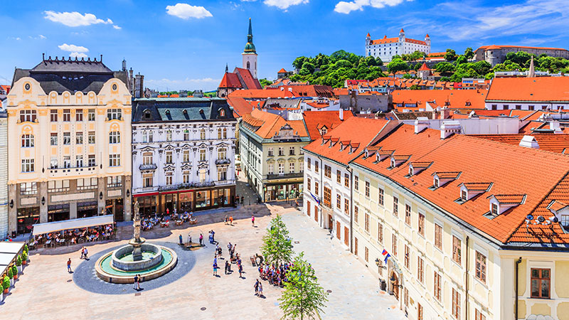 Gamle og rverdige bygninger i sentrum av Bratislava. Stor plass med statue og mange mennesker. 