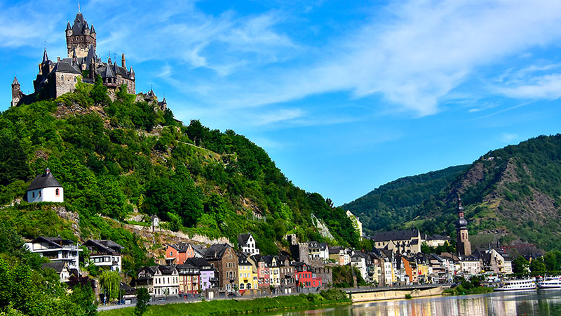 En mektig borg på toppen av en ås med byen Cochem beliggende nedenfor. Båter på Rhinen. 