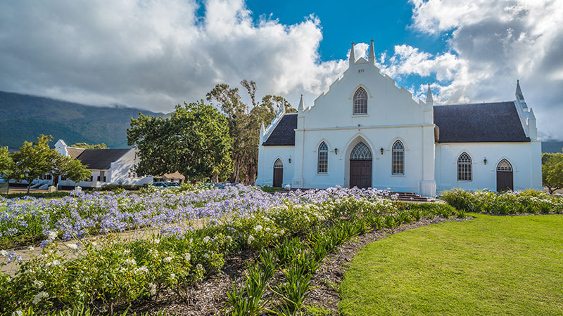 Hvit kirke med lilla blomster foran i Franschhoek