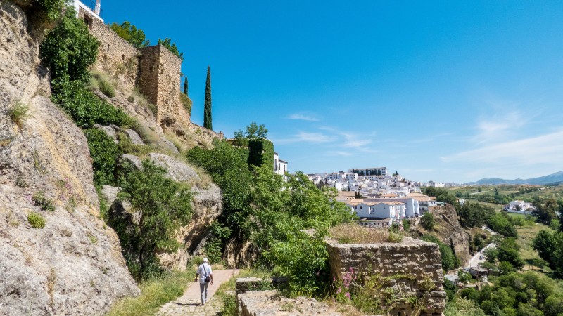 en mann som g�r p� en sti med bygninger og en festning p� toppen av fjellet