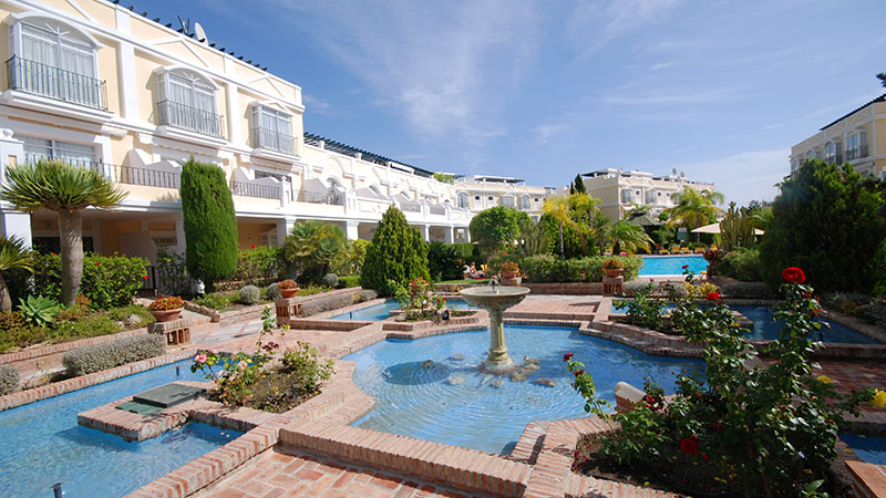 En stor hage med fontener og små svømmebasseng. Omkranset av leiligheter.