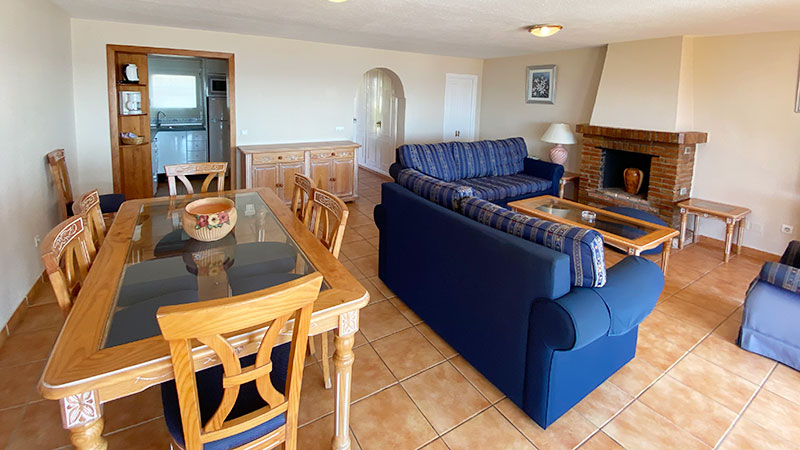 Stue med sofagruppe, peis og spisebord. Utsikt inn mot kjøkken.