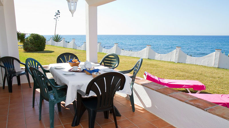 Dekket spisebord på terrasse. To solsenger og utsikt mot havet.