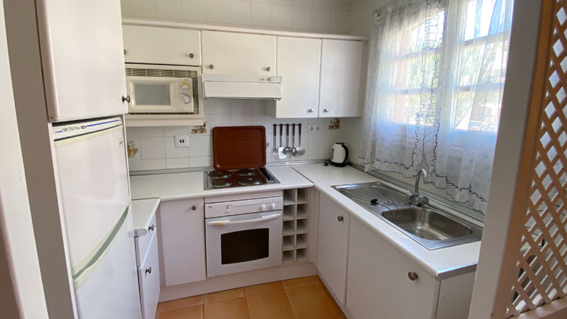 Hvitt kjøkken med vaskekum, komfyr, skap og kjøleskap.