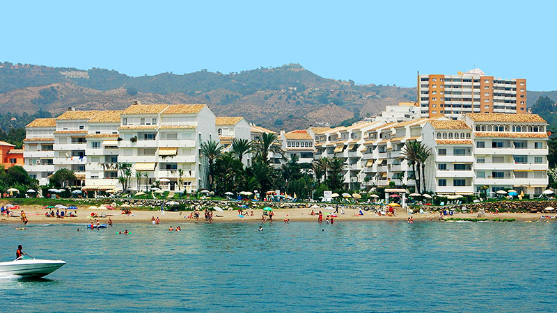 Hotell Club Playa Real me strand og hav i forkant. Fjell i bakgrunnen.