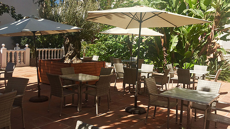 Flere bord med stoler på utendørs terrasse. Skygger godt for solen. 