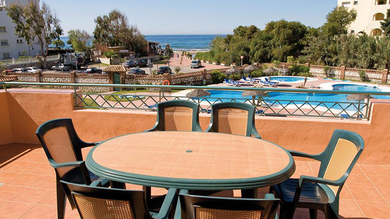 Bord med stoler på terasse med utsikt mot svømmebasseng og havet.