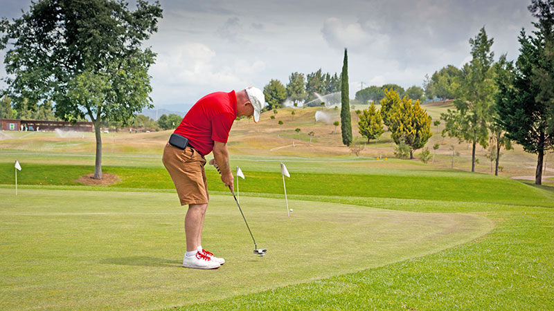 Man i rød skjorte trener på golfputting i Marbella.