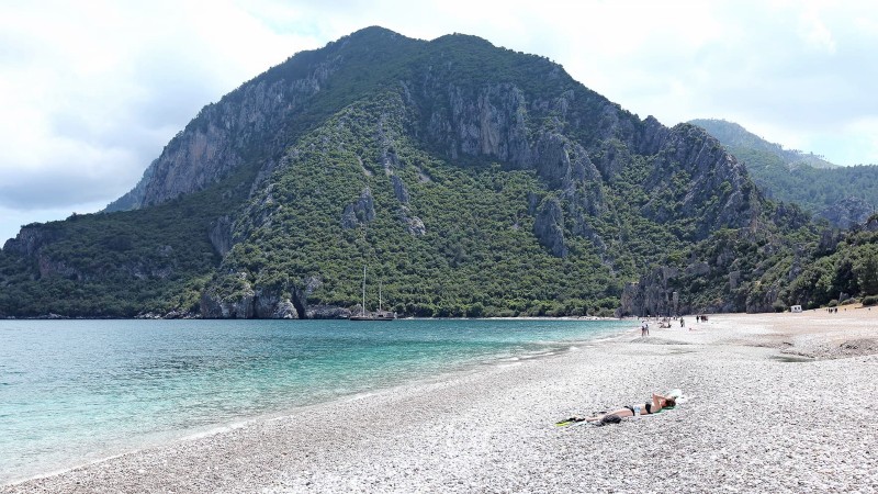 Strand, fjell, hav og mennesker som koser seg p stranden